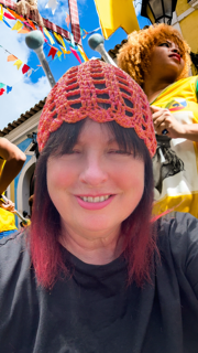 Crochet Skull Cap Smiling woman with a red crocheted hat at a festive outdoor event.